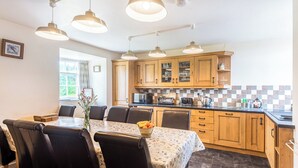 A kitchen with wooden cabinets, a dining table with chairs, and pendant lights. - Well Farmhouse - UK11880 (Holsworthy, near Launceston)