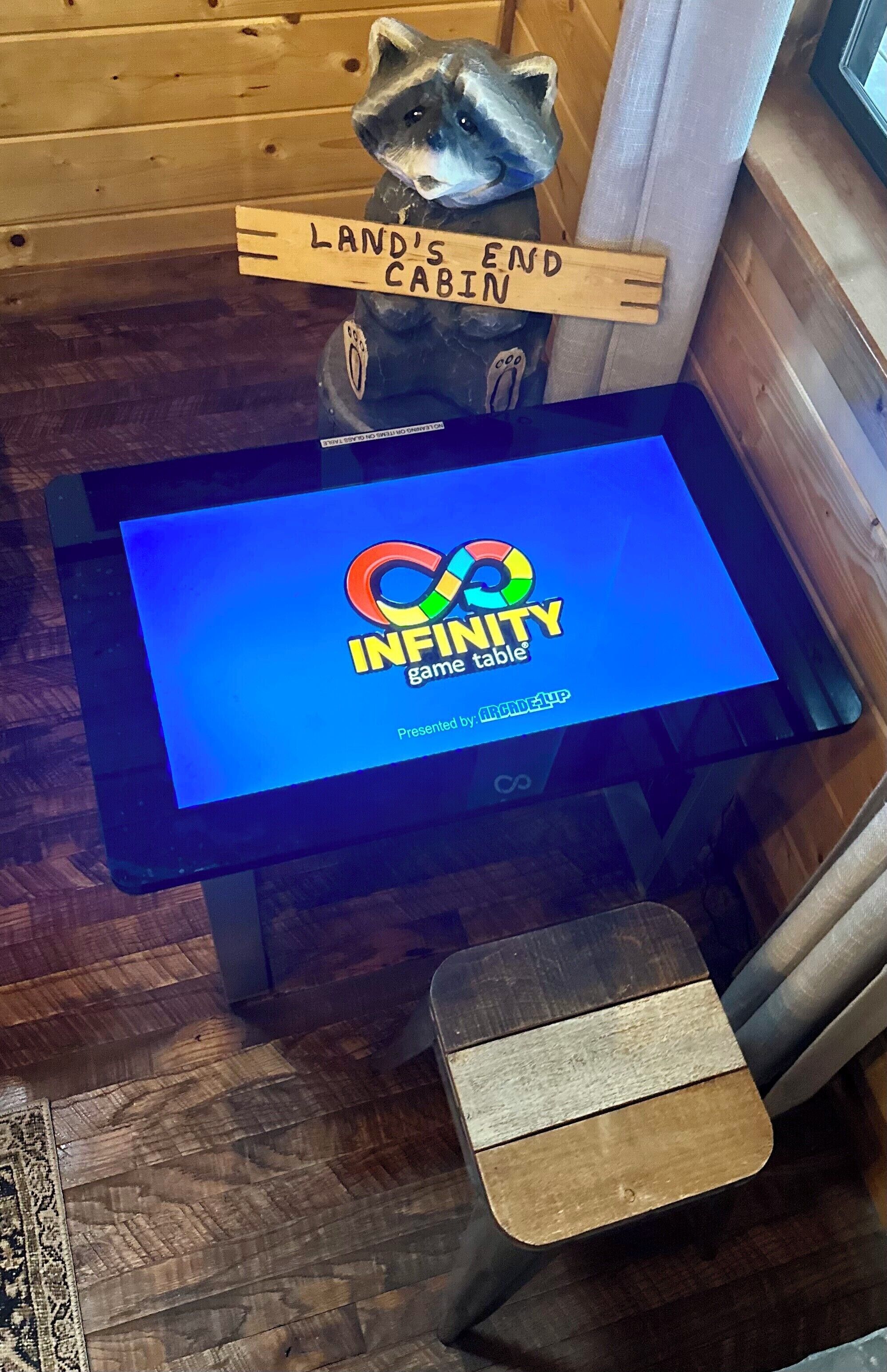Una tableta mostrando el logotipo del juego Infinity, una figurita de mapache y un letrero que dice 'Land's End Cabin'.