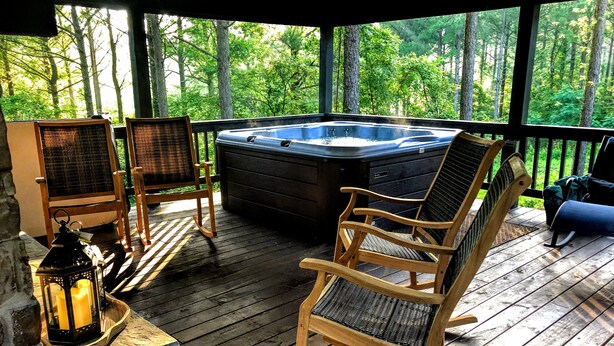 Una terraza de madera con un jacuzzi, mecedoras y un farol.