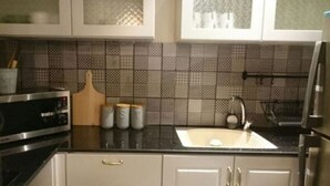 Una cocina con encimera negra, electrodomésticos de acero inoxidable, salpicadero de azulejos y armarios blancos.