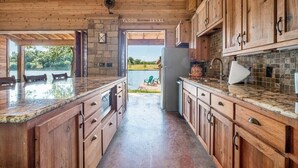 A spacious kitchen with wooden cabinets, granite countertops, and a stone backsplash. - Casita Grove-2 Lakeside Homes w/Casita & Boat Lift (Burnet)
