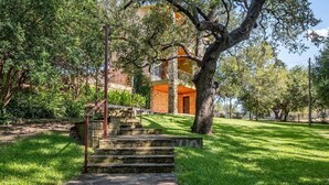 A stone staircase leading to a building with a red door, surrounded by lush greenery and trees. - Casita Grove-2 Lakeside Homes w/Casita & Boat Lift (Burnet)