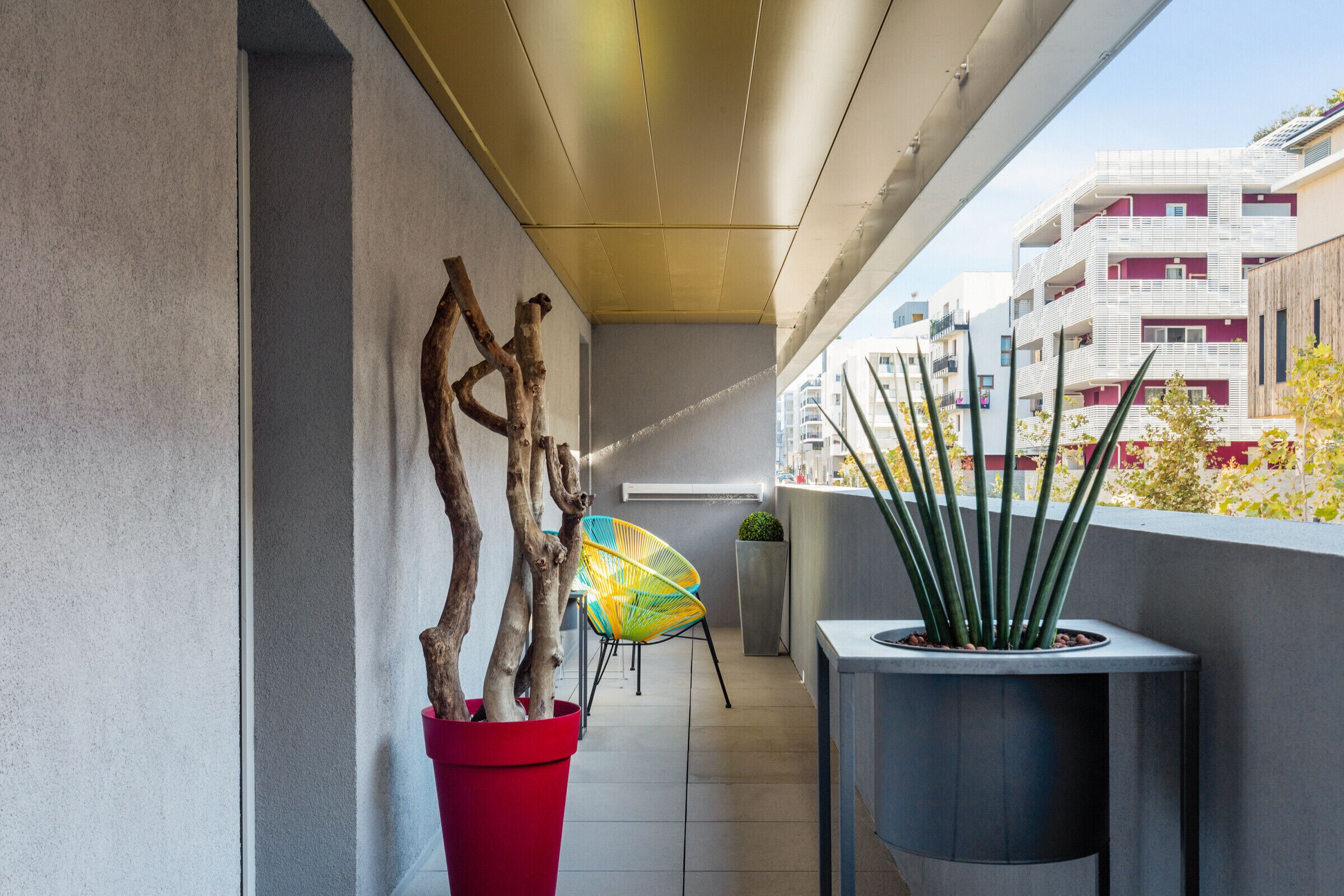 Ein moderner Balkon mit einem Topfpflanzen, einem bunten Stuhl und Blick auf Gebäude.