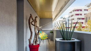 A modern balcony with a potted plant, a colorful chair, and a view of buildings. - Luminescence Parc Marianne (Montpellier)