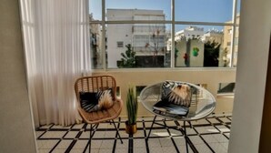 Una habitación con un ventanal grande, dos sillones de mimbre, una planta en maceta y suelo de baldosas.