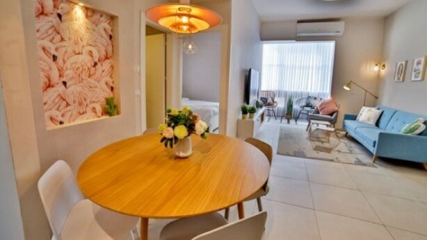 Una sala de estar moderna con una mesa de comedor redonda de madera, sillas blancas, un sofá azul y un amplio ventanal con persianas.