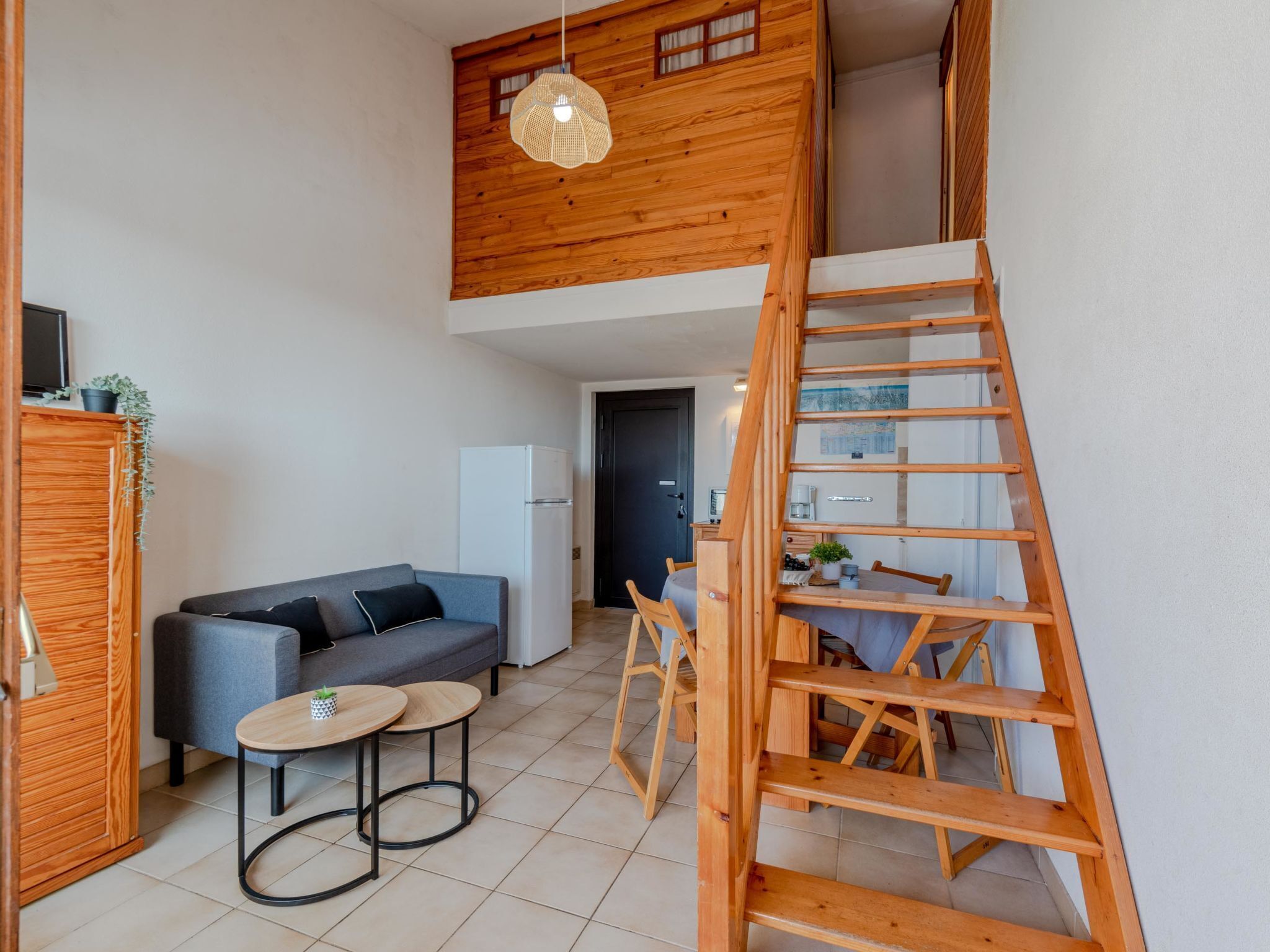 A compact living space with a loft area, a sofa, a small table, and a wooden ladder.