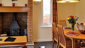 A cozy dining area with a brick fireplace, wooden table, chairs, and a vase with flowers.