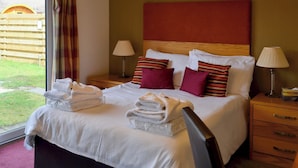 A hotel room with a bed, two bedside tables, a window with curtains, and a view of the outside.