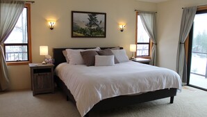 A neatly made bed with white linens and multiple pillows, two bedside lamps, a nightstand, and a framed landscape painting on the wall. - Ski Hill home w/ stunning views & hot tub! (Leavenworth)