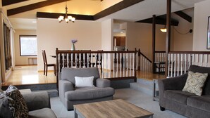 A spacious living room with a grey sofa, a wooden coffee table, and a staircase with white balusters. - Ski Hill home w/ stunning views & hot tub! (Leavenworth)