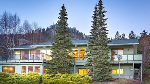 A two-story house with a balcony, surrounded by evergreen trees and a well-maintained lawn. - Ski Hill home w/ stunning views & hot tub! (Leavenworth)