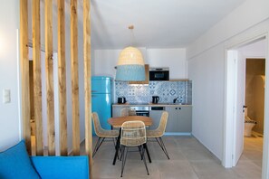 A compact kitchen with a dining area, featuring a blue refrigerator, a wooden dining table with wicker chairs, and a hanging light fixture.
