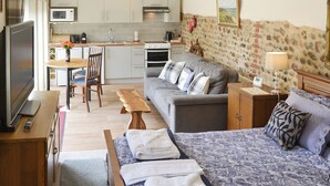 Ein kompaktes Hotelzimmer mit Küchenzeile, Schlafsofa, Fernseher und Bett mit gemustertem Überwurf.