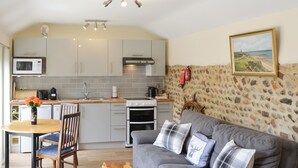 Ein kompakter Wohnbereich mit Küchenzeile, grauem Sofa mit karierten Kissen, Holztisch und einer Wand im Steinoptik.