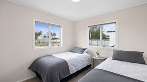Une chambre avec deux lits, une petite table de chevet avec une lampe, et de grandes fenêtres donnant sur l’extérieur.
