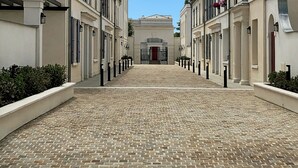 Ein Kopfsteinpflasterweg führt zu einem Gebäude mit roter Tür, gesäumt von weißen Gebäuden mit schwarzen Fensterläden.