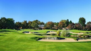 Ein Golfplatz mit Sandbunkern, einem Teich und Bäumen im Hintergrund.
