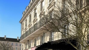Ein Gebäude im klassischen Baustil, mit einem Balkon mit schwarzen Geländern und einer überdachten Außenbereich-Sitzgelegenheit mit Blumentöpfen.