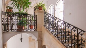 A staircase with ornate black railings, potted plants on the landing, and a hanging lantern. - In Naca - Castello Maniace Ortigia Wifi (Siracusa)