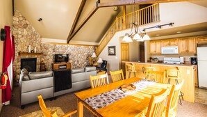 Una sala de estar acogedora con chimenea de piedra, un sofá y una mesa de comedor de madera.