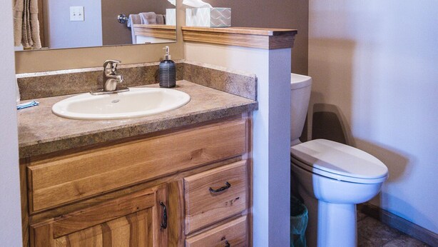 Un baño con tocador de madera, lavamanos, espejo y retrete.