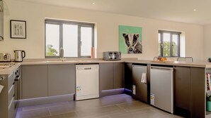 Una cocina moderna con armarios grises, lavavajillas, cafetera y tostadora. Hay dos ventanas que dejan entrar luz natural.