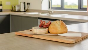 Una encimera de cocina con una tabla de cortar que sostiene un queso entero, uvas y una hogaza de pan.