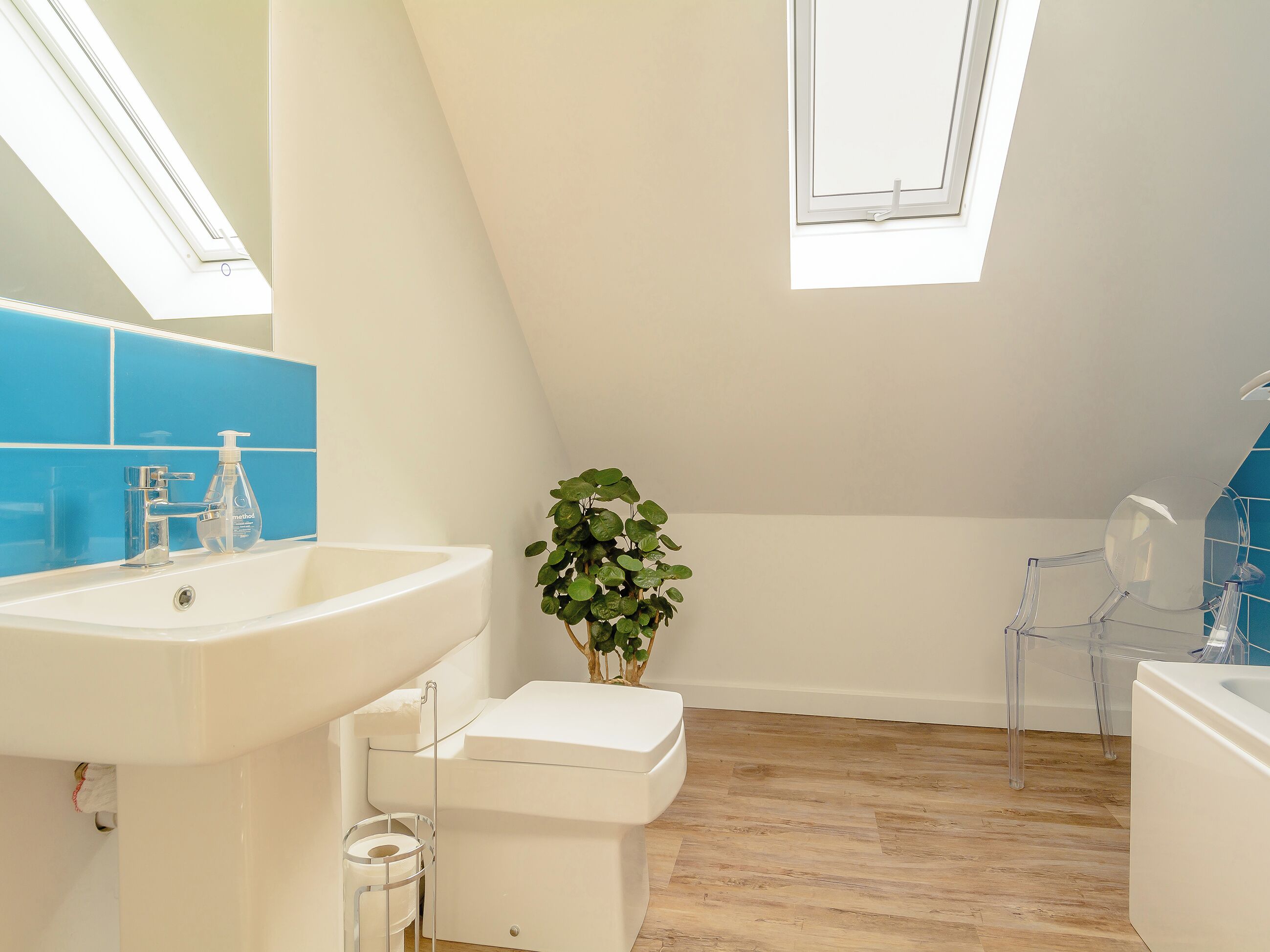 Une salle de bain moderne avec un puits de lumière, un lavabo blanc, des toilettes et une chaise transparente.
