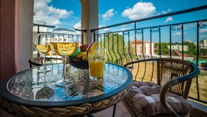 A balcony with a glass table holding two glasses of white wine, a bowl of fruit, and a glass of orange juice. - Step (Sunny Beach)