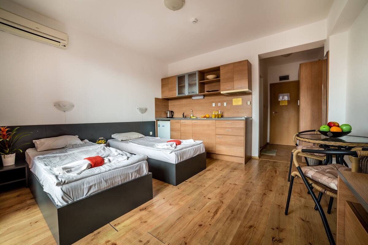 A modern bedroom with two beds, a kitchenette, and a dining area.