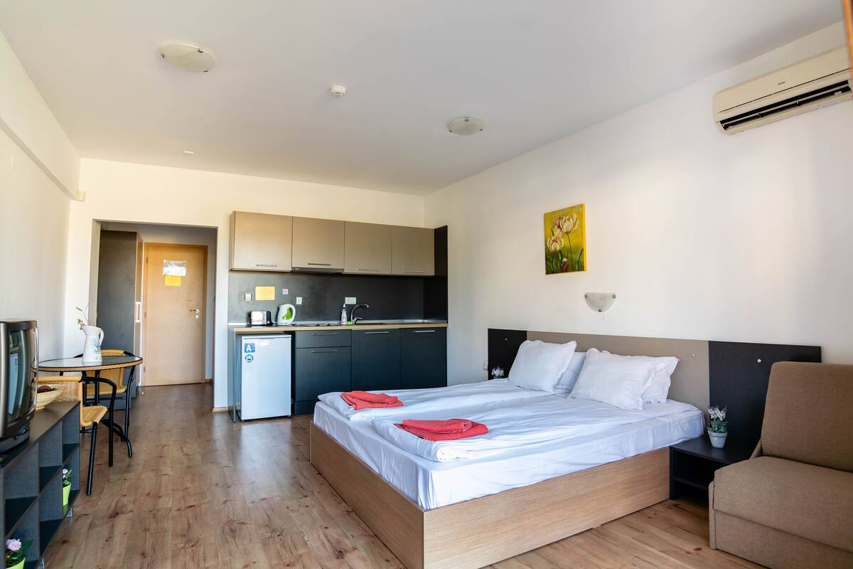 A hotel room with a wooden bed, a small kitchenette, a dining table, and a TV.