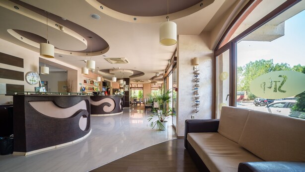 A modern hotel lobby with a curved reception desk, a seating area, and a large window offering a view of the street. - Step (Sunny Beach)