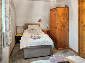 A bedroom with a bed, a wooden wardrobe, a bedside table with a lamp, and a radiator.