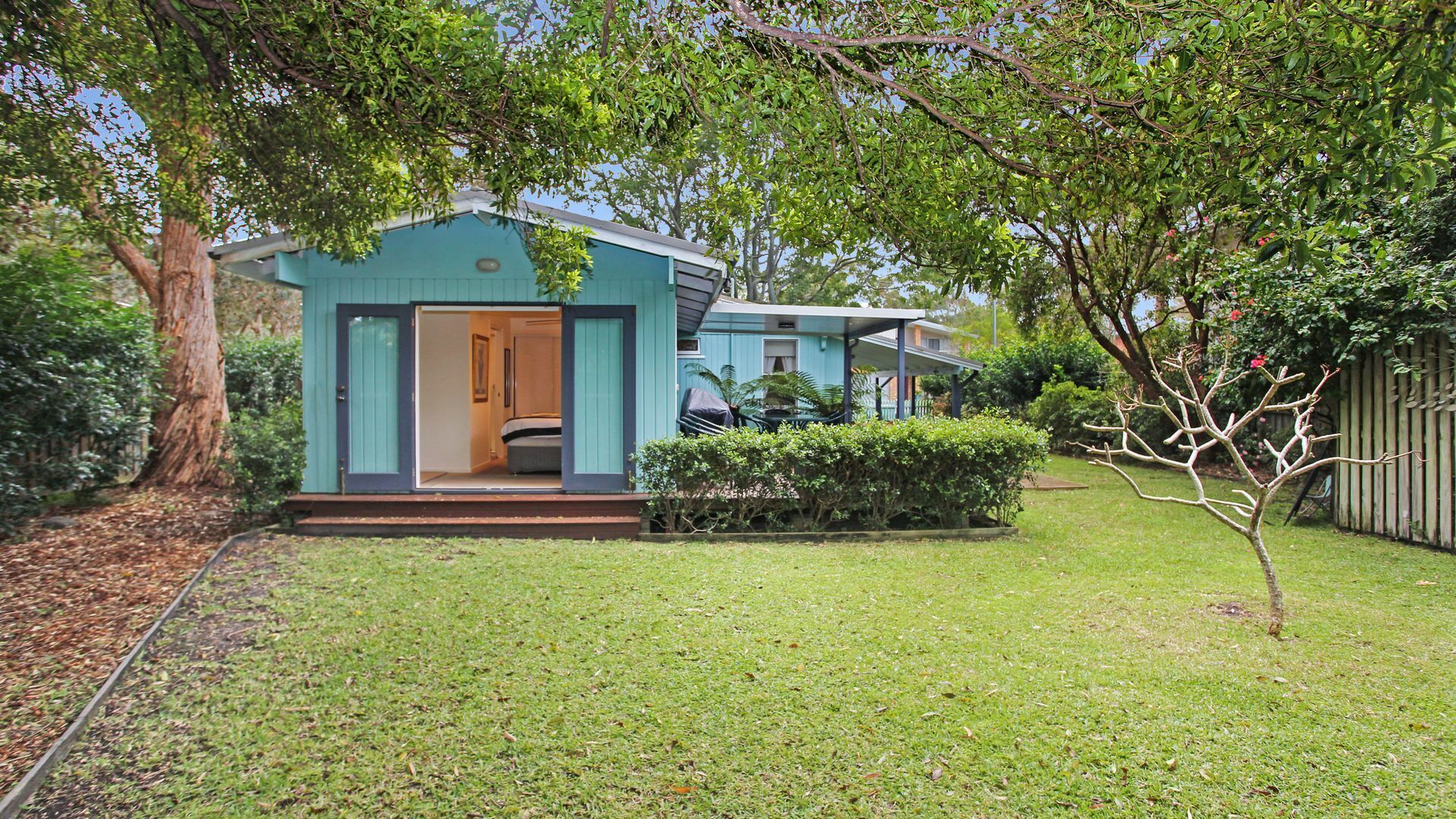 A small, single-story house with a front porch and a visible bedroom.