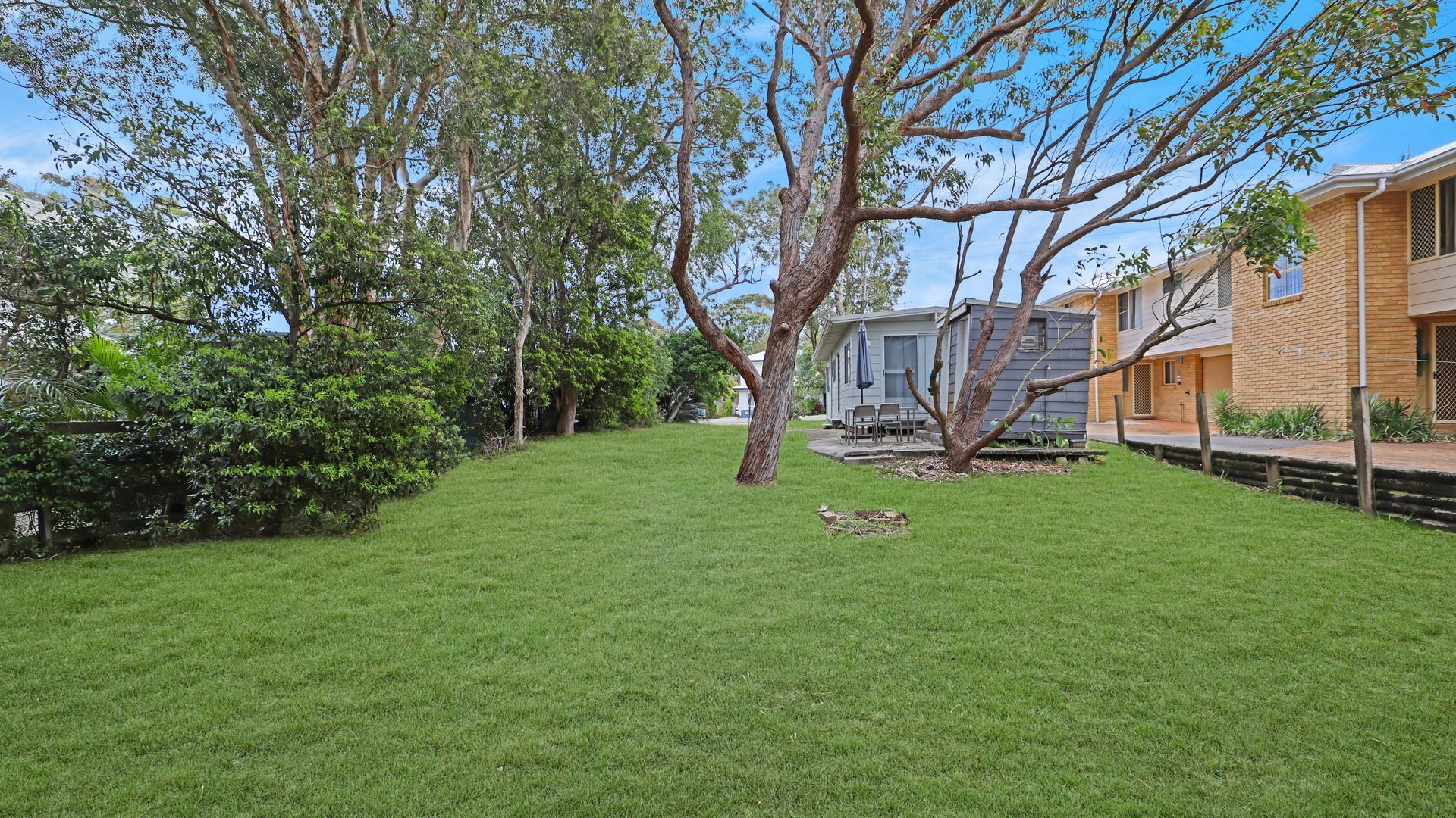 A well-maintained grassy yard with mature trees and a small patio area.