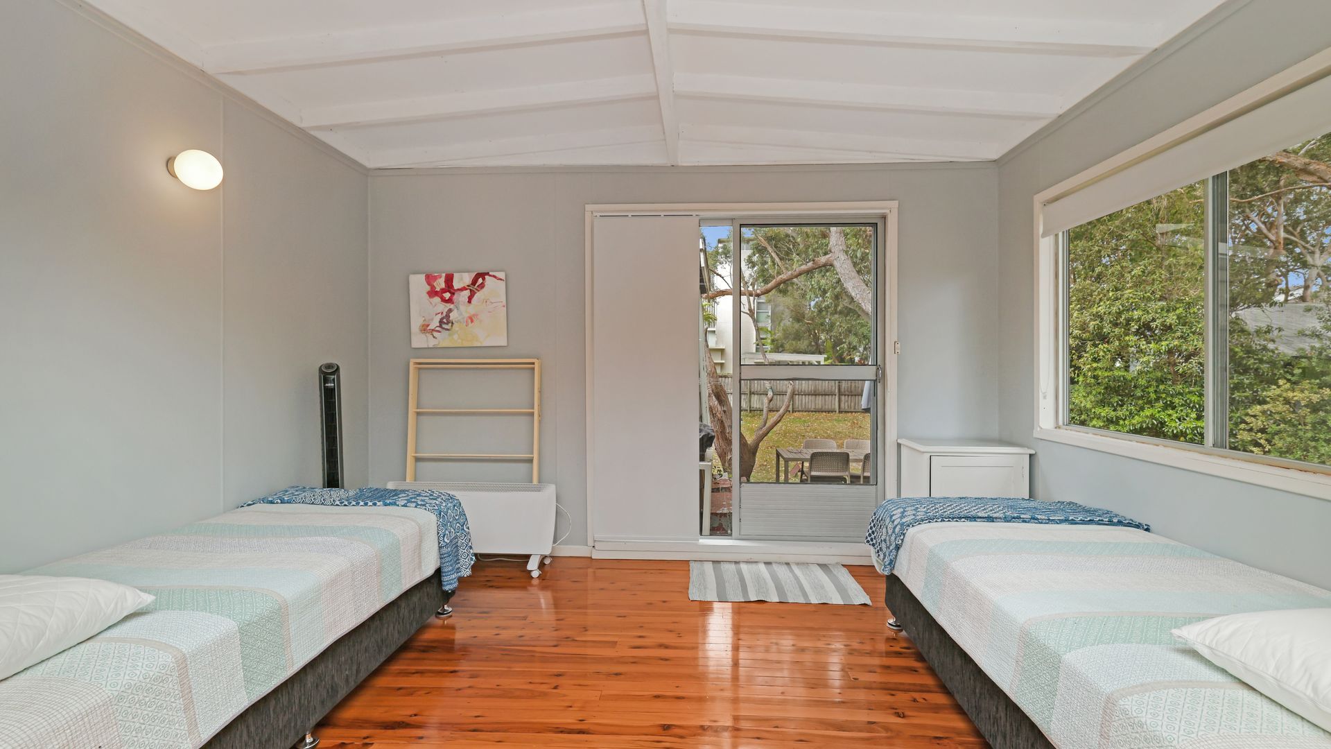 A bedroom with two beds, a window, a door leading outside, and a small shelf.