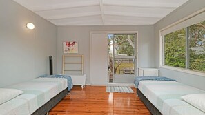 A bedroom with two beds, a window, a door leading outside, and a small shelf.