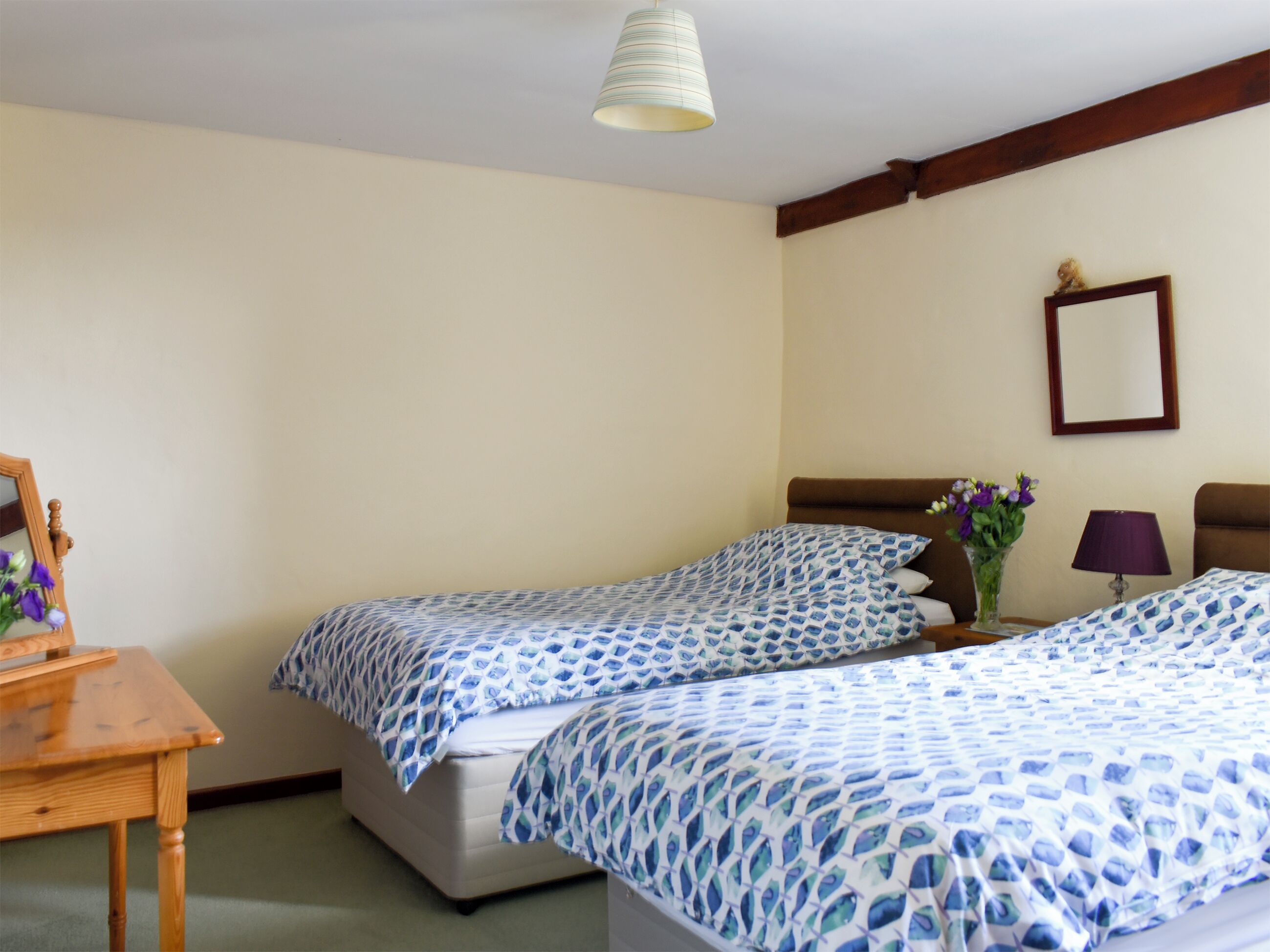 Une chambre d’hôtel avec deux lits, une table de chevet en bois, un miroir et un luminaire suspendu.