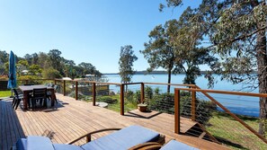 A wooden deck with a table and chairs, overlooking a lake with a boat in the distance. - Paradise - 54 Eastslopes Way (North Arm Cove)