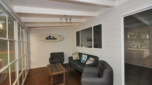 A cozy room with a wooden table, two armchairs, and a sofa. There is a surfboard decoration on the wall and a large window.