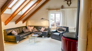 Een loft-achtige woonkamer met een schuine plafond, een leren zwarte bank, een glazen salontafel en een rode kast.