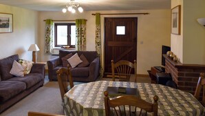 A living room with a sofa, chairs, a dining table, a fireplace, and a window with curtains. - Trewin Court - UK11878 (Holsworthy, near Launceston)