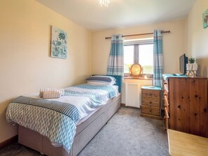 A bedroom with a bed, dresser, window with curtains, radiator, and a painting on the wall.