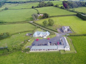 An aerial view of a rural property with a large house, a barn, and several parked cars.