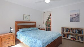 Ein Schlafzimmer mit Bett, Nachttischen, einem Bücherregal, einem Fenster mit Vorhängen und einem Deckenventilator.