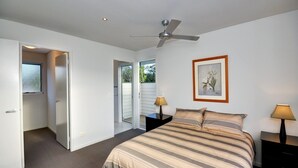 A bedroom with a bed, two bedside tables, a ceiling fan, a door leading to a balcony, and a framed picture on the wall.