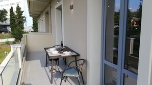 A balcony with a table set for two, chairs, and a glass door leading to a garden. - Casa Marina apartment  kontokali  (Kontokali)