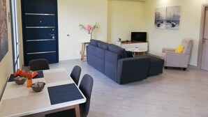 A modern living room with a sofa, a dining table with chairs, a TV, and artwork on the wall. - Casa Marina apartment  kontokali  (Kontokali)