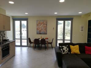 A modern living room with a sofa, a dining table with chairs, and a kitchen area with cabinets and an oven.